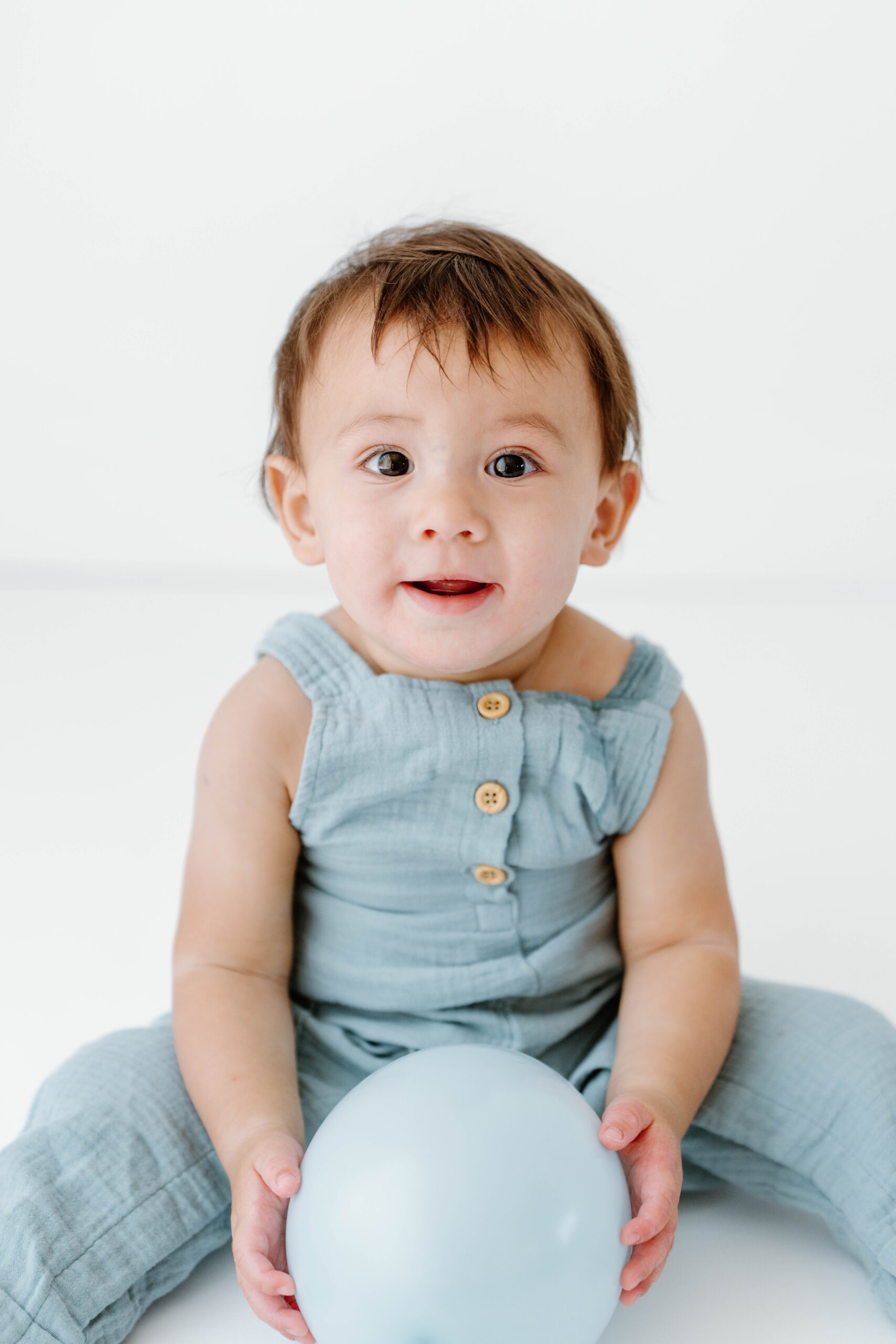 Zachary sits with a blue balloon in a light blue romper in our natural light studio