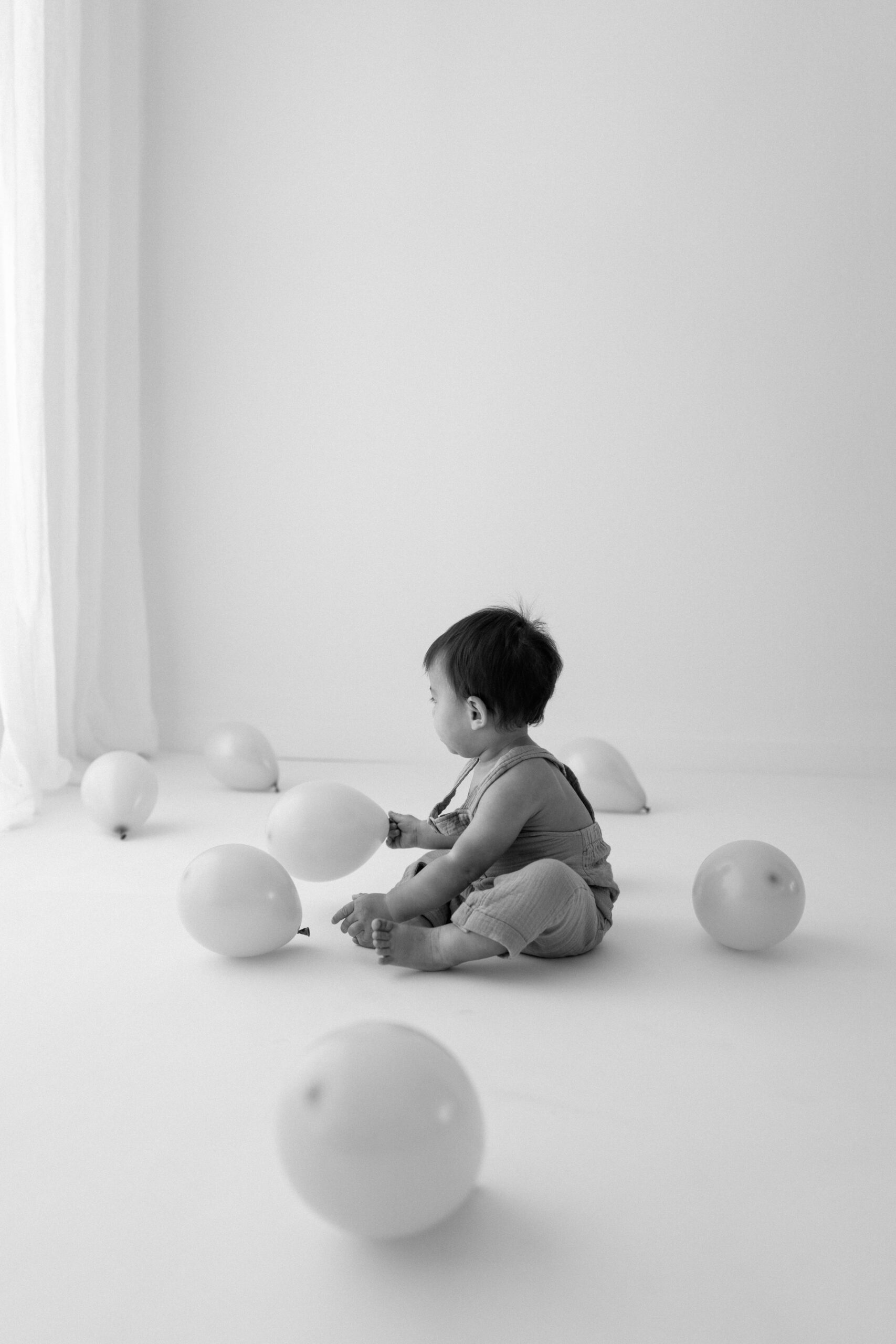 Black-and-white photo of Zachary playing among balloons in the white studio