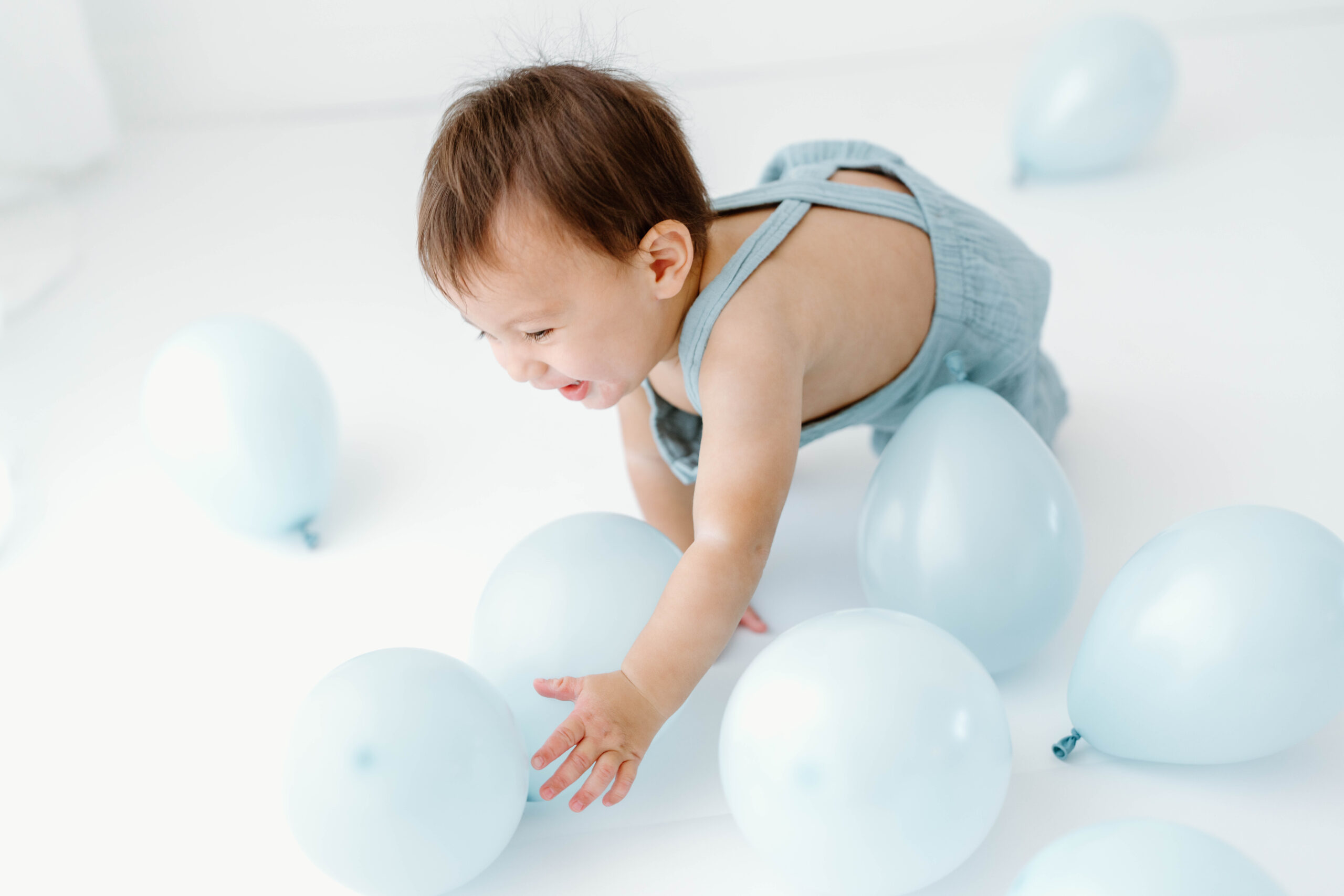 Zachary reaches for pale blue balloons on the studio floor