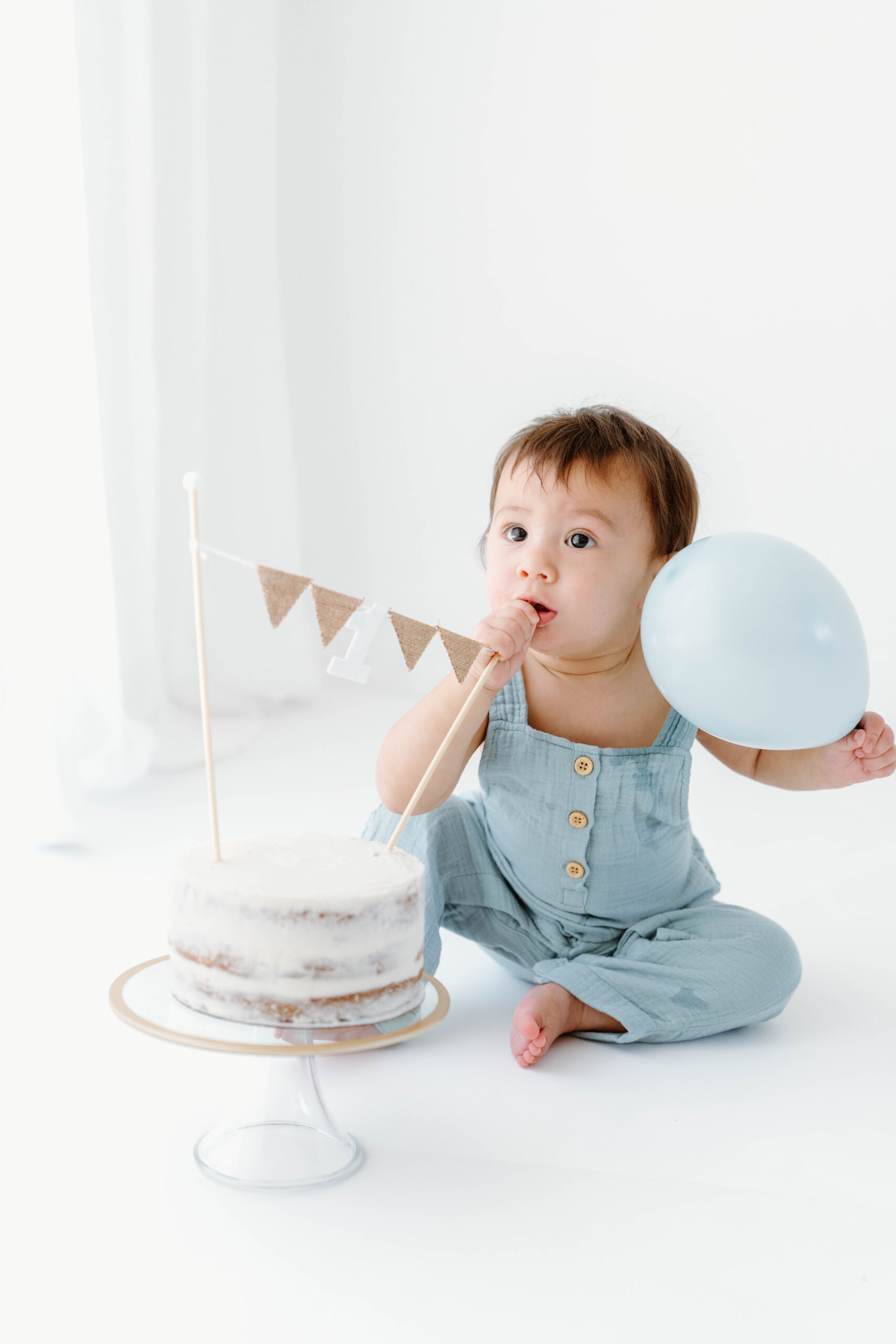 Zachary licks frosting from his fingers beside his first birthday cake