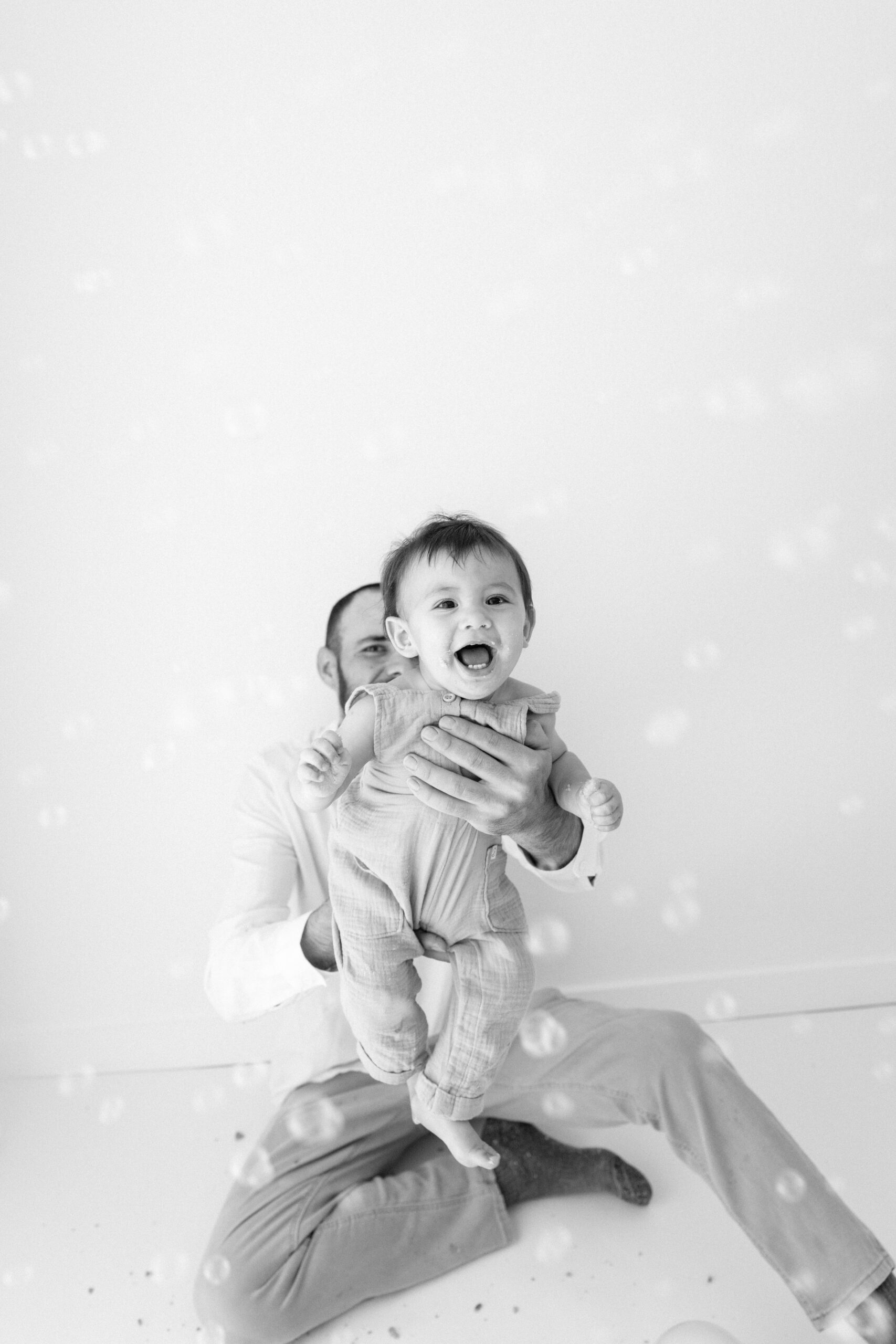 Black-and-white photo of Zachary held up by his dad among bubbles