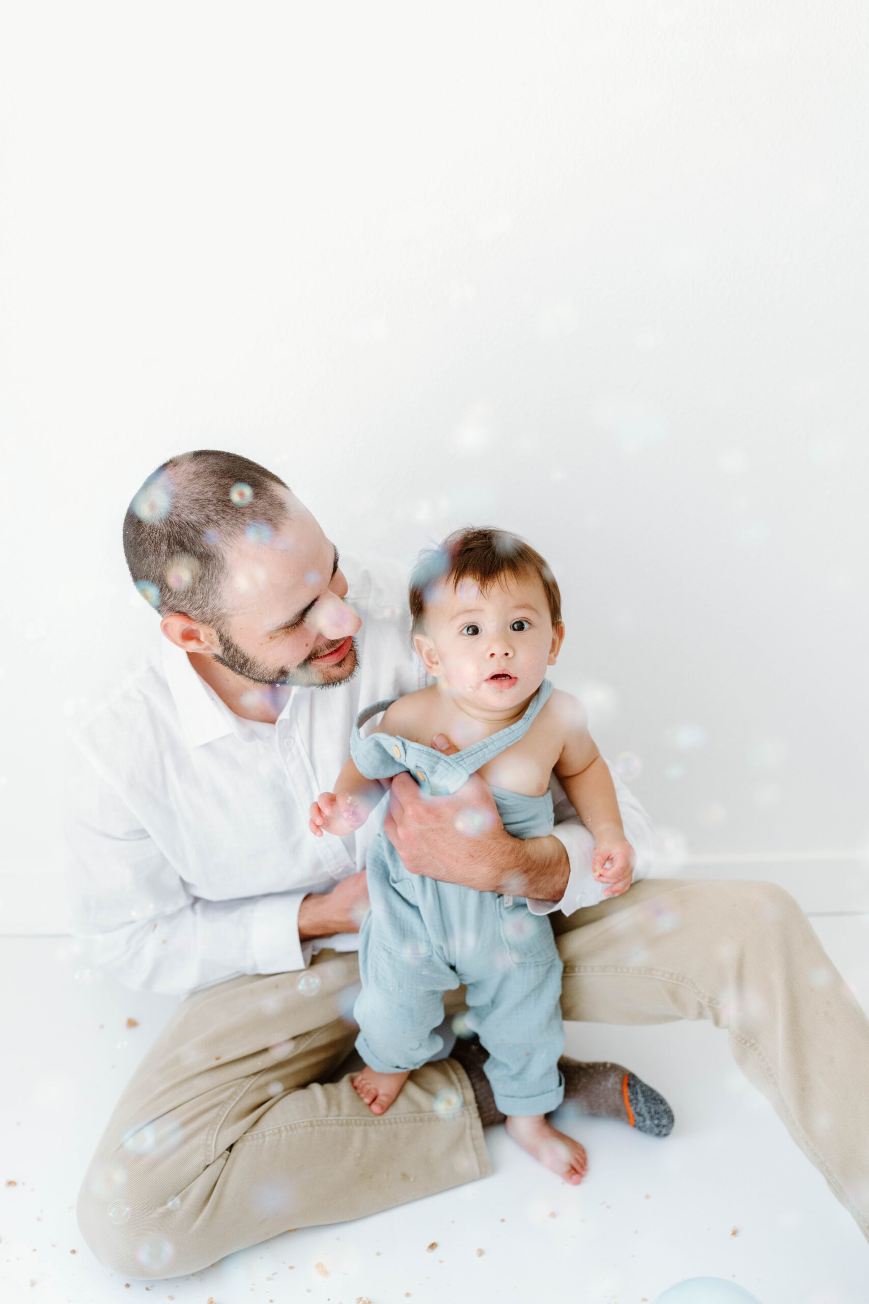 Zachary stands on his dad's lap among the bubbles