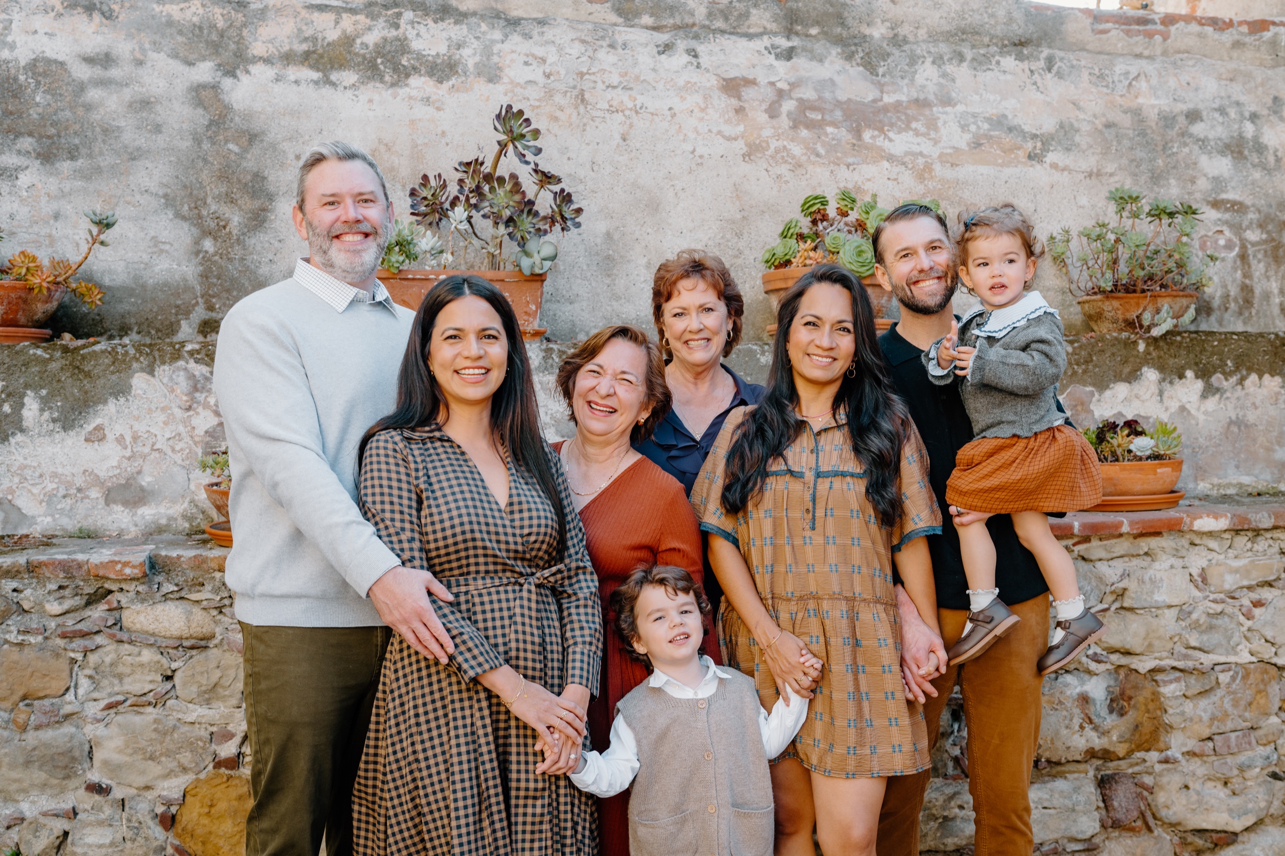 Extended family smiling in front of the bell wall at Mission San Juan Capistrano