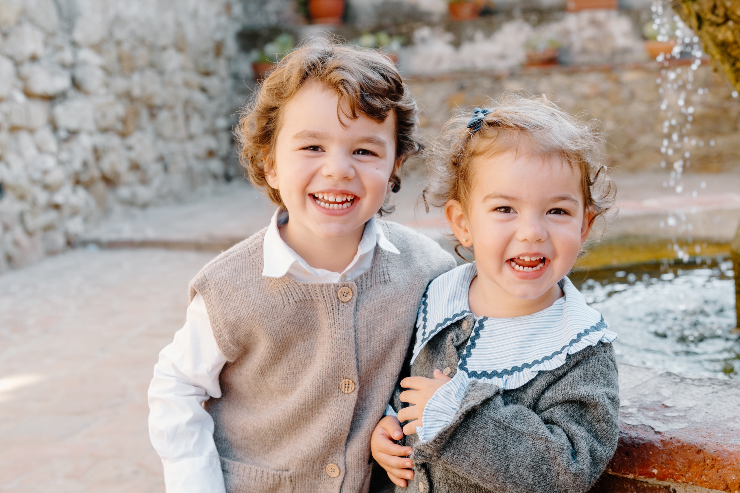 Little boy and toddler girl laughing cheek to cheek by a fountain