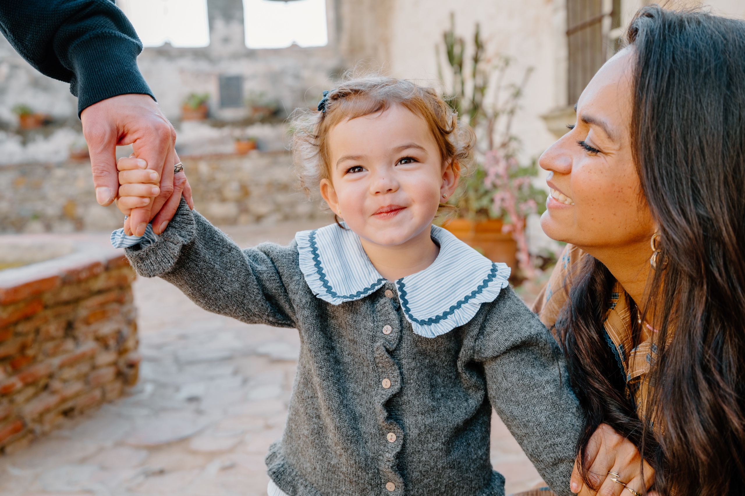 Toddler girl holding a hand and smiling in a Mission courtyard
