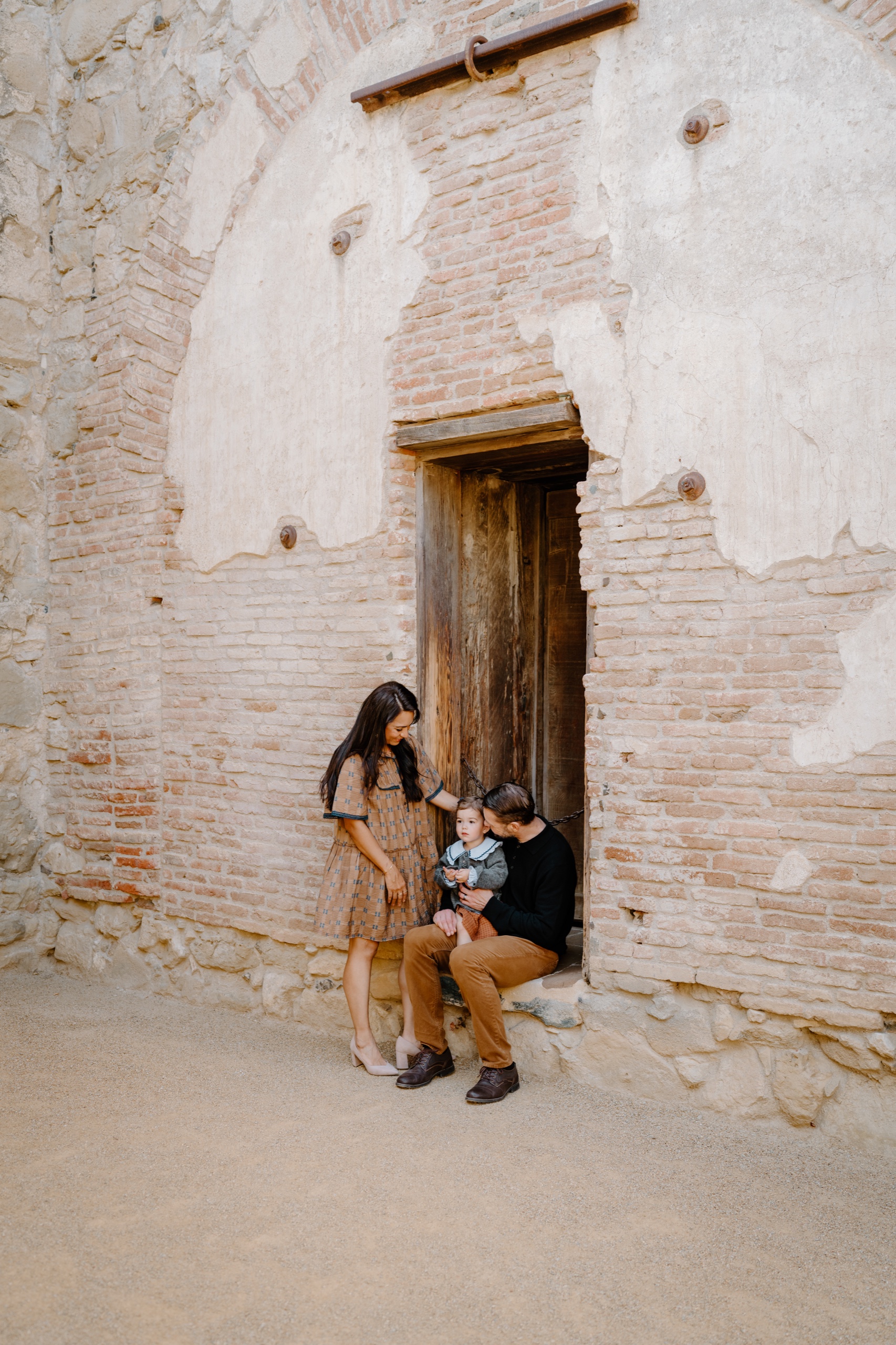 Young family sitting together in a weathered wooden doorway at the Mission