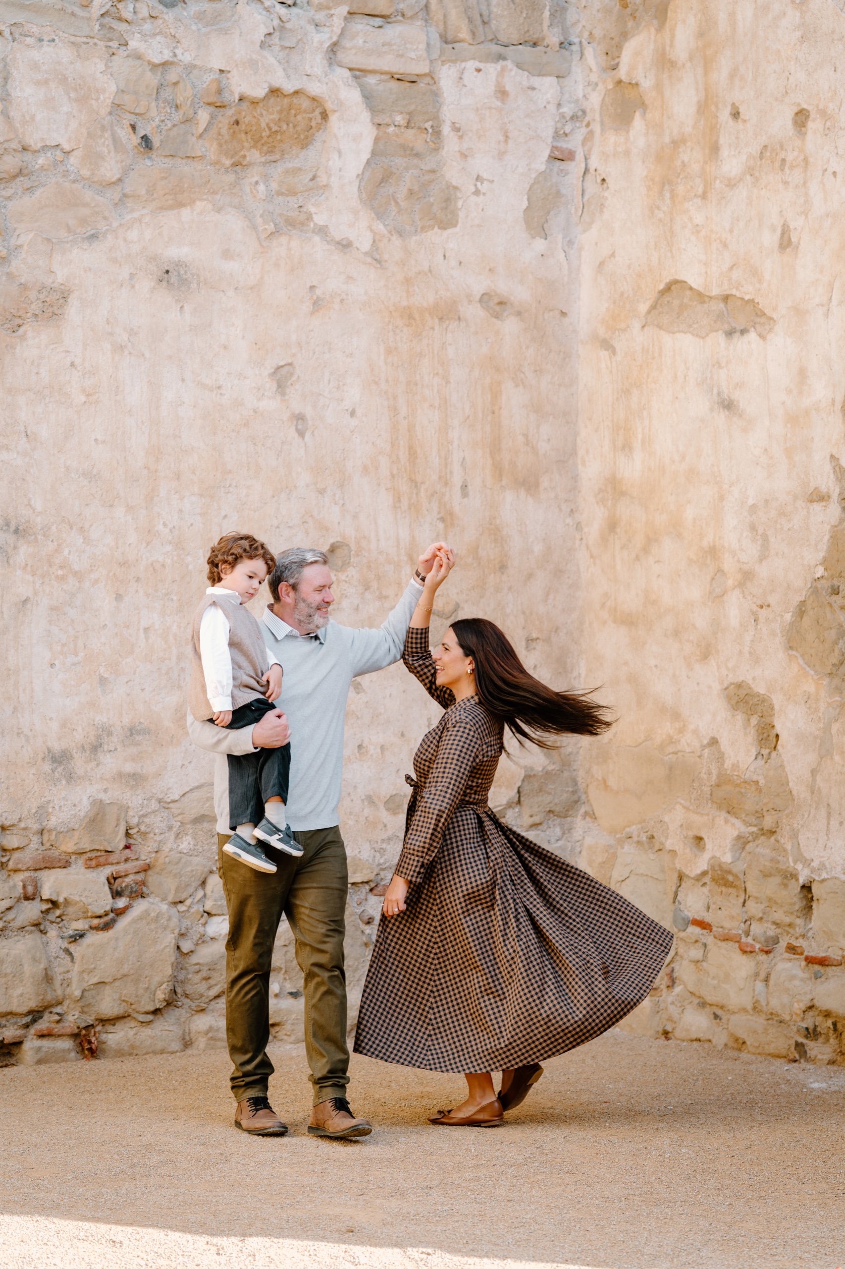 Woman twirling her dress while a man holds a child up against an adobe wall