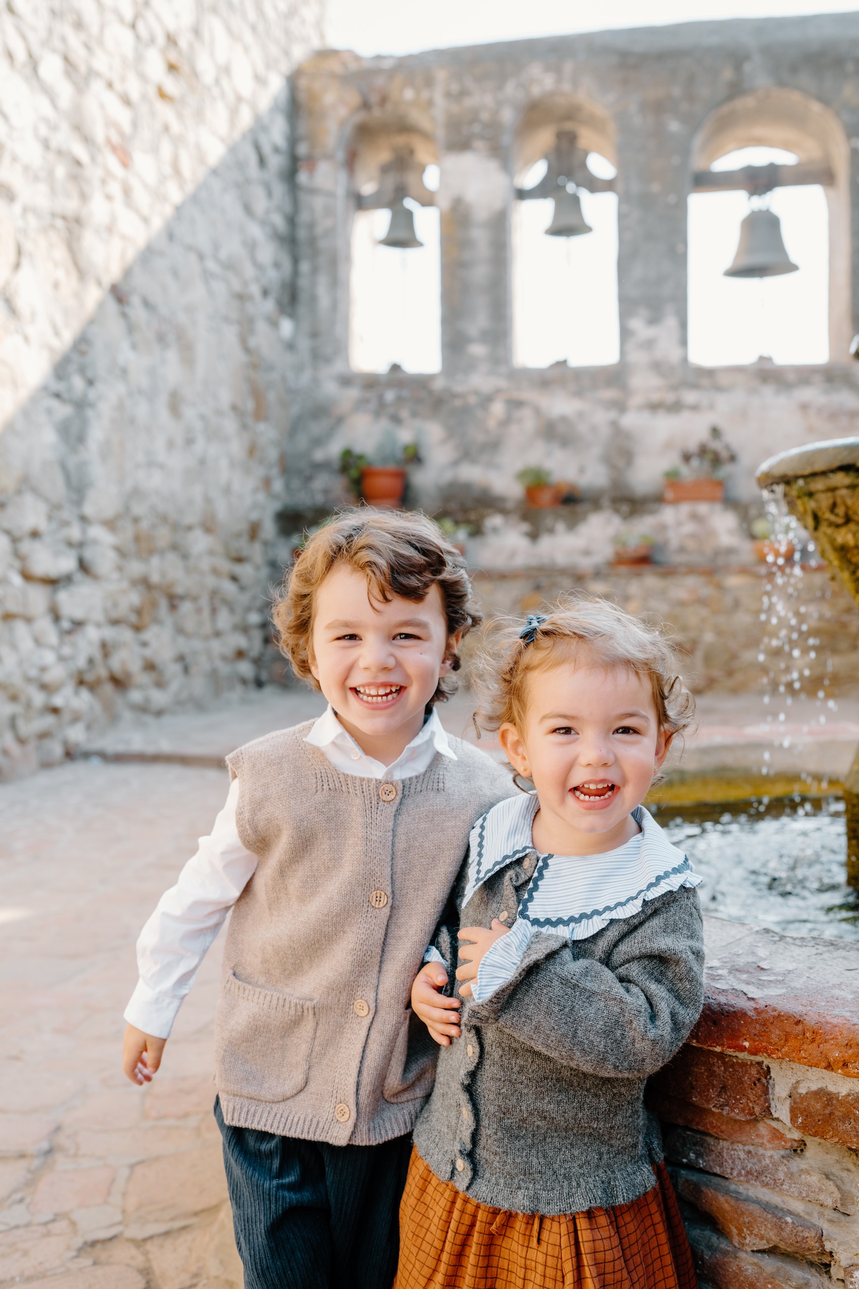 Little boy and toddler girl hugging and laughing beside a fountain at Mission San Juan Capistrano