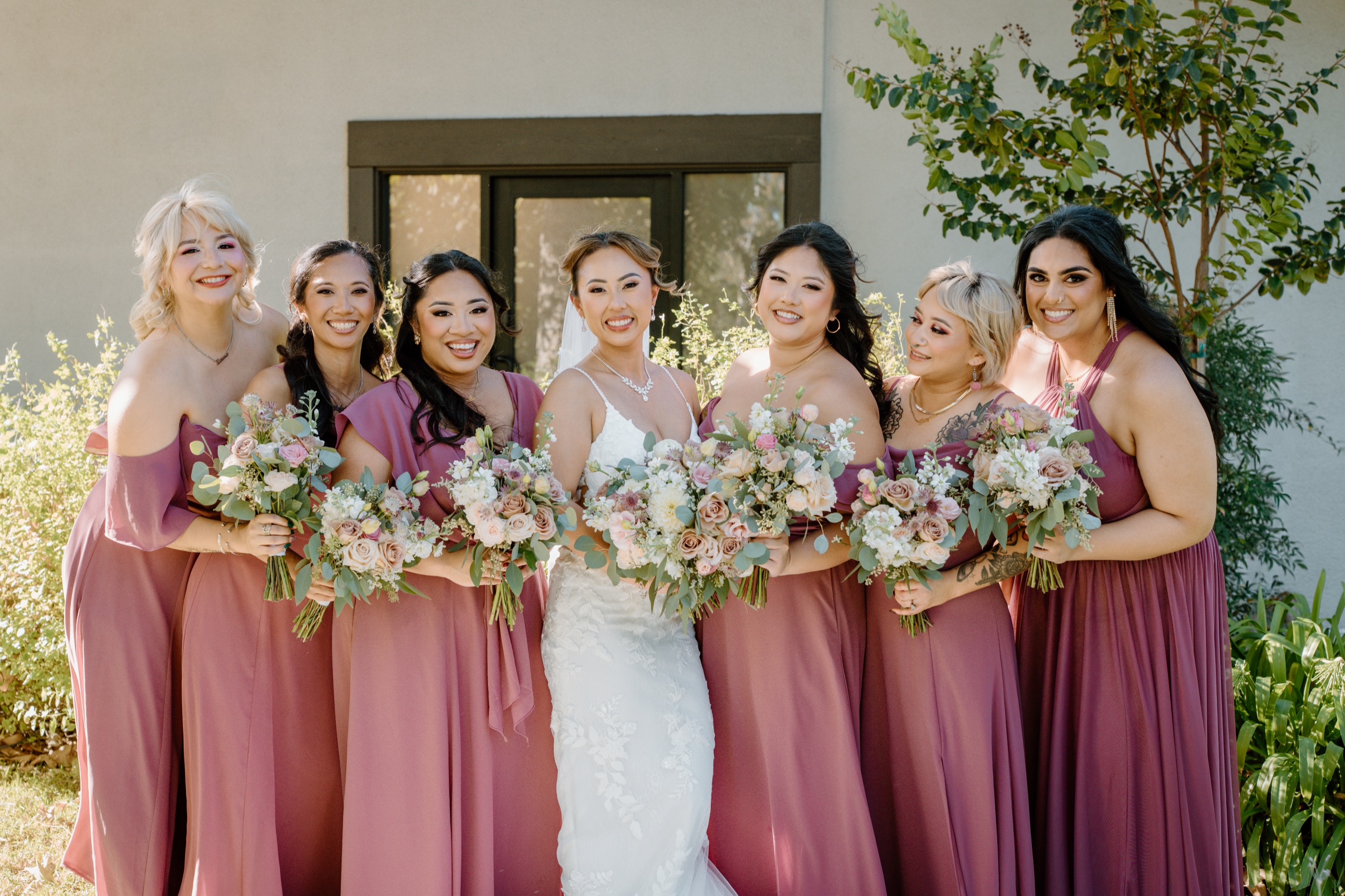 Bride with her bridesmaids in dusty rose dresses holding pink and white bouquets