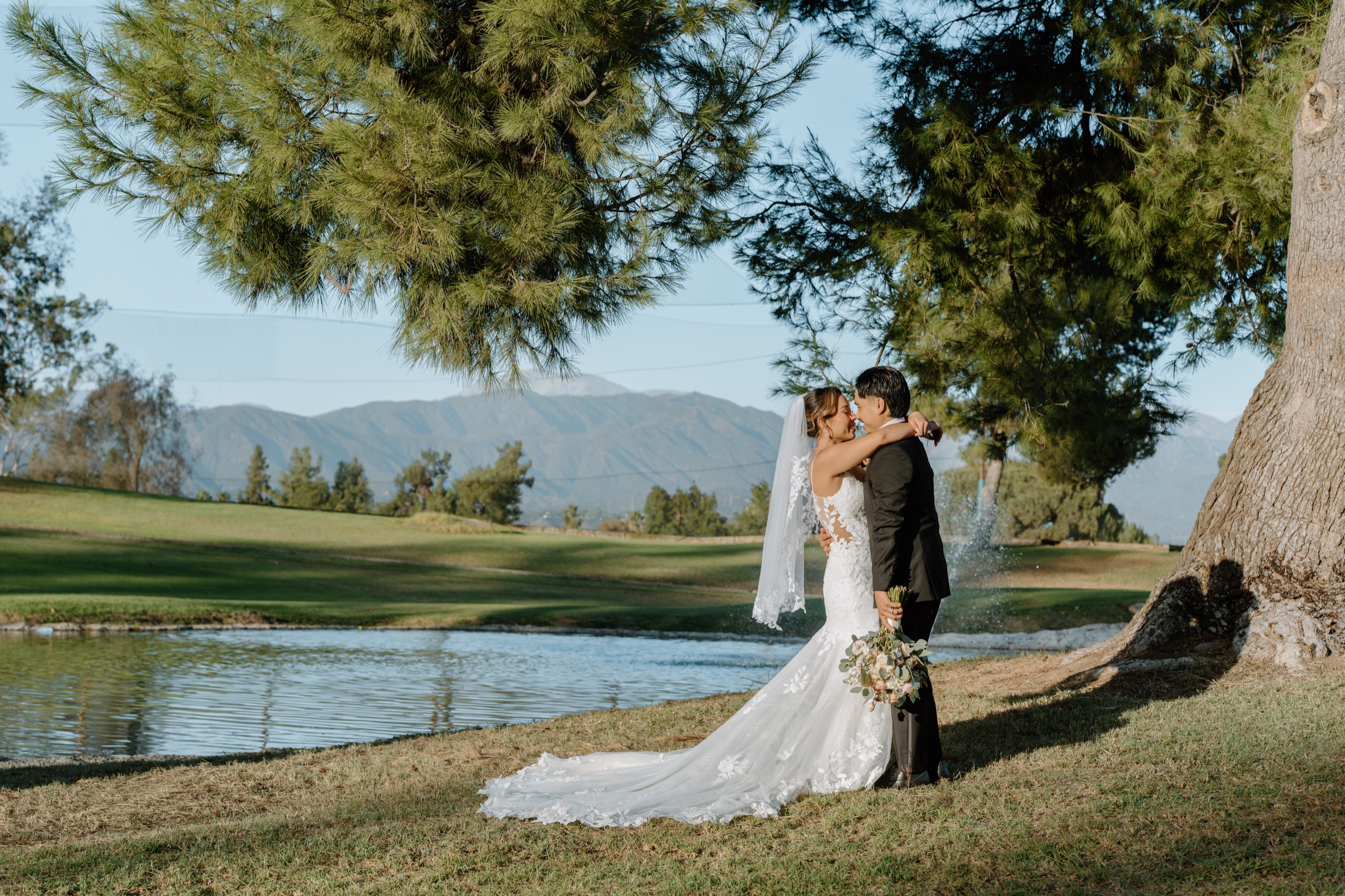 Bride and groom embracing by the lake at Mountain Meadows Golf Course with mountains behind