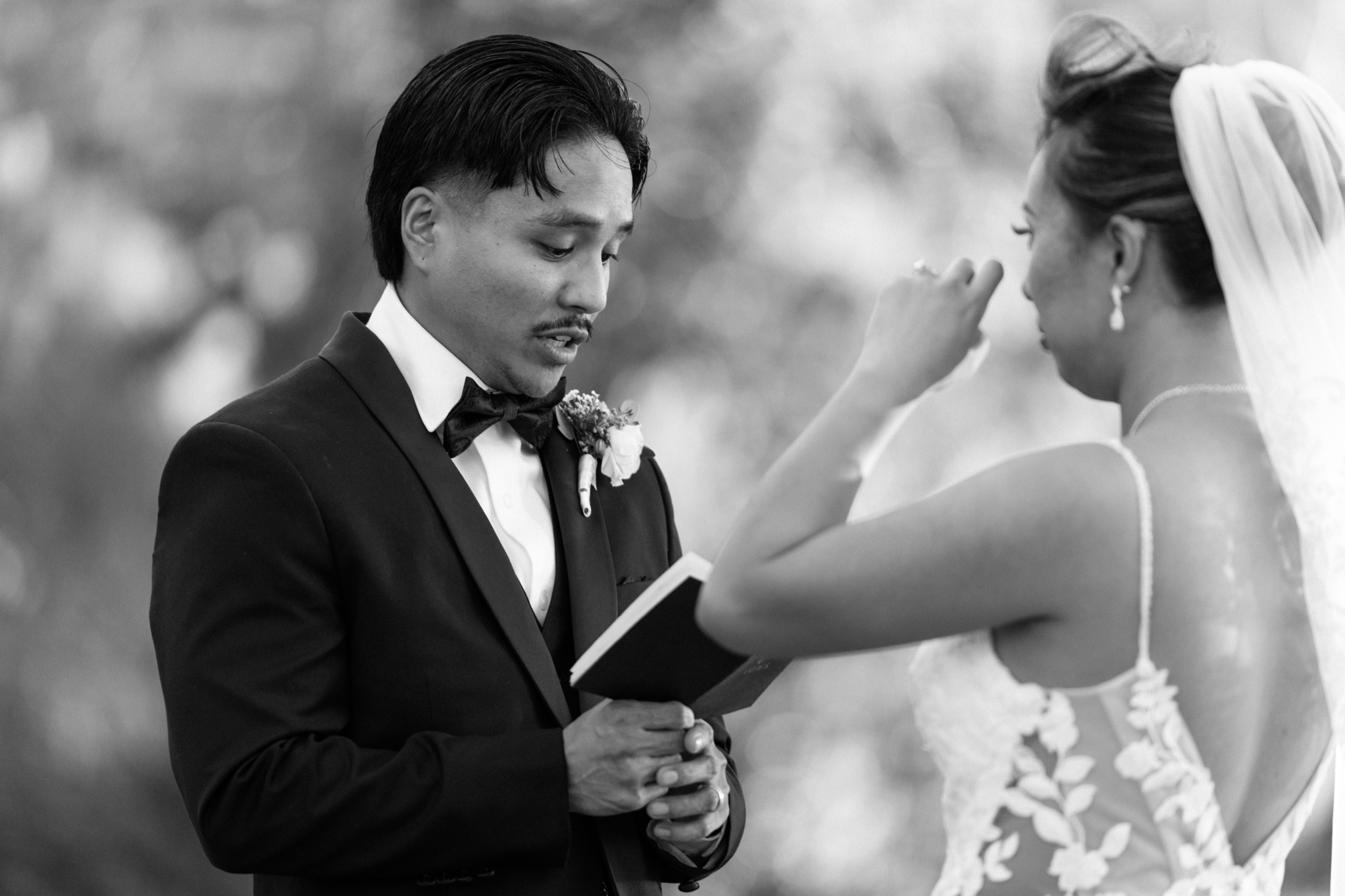 Groom reading from a small book as the bride wipes away a tear during the ceremony