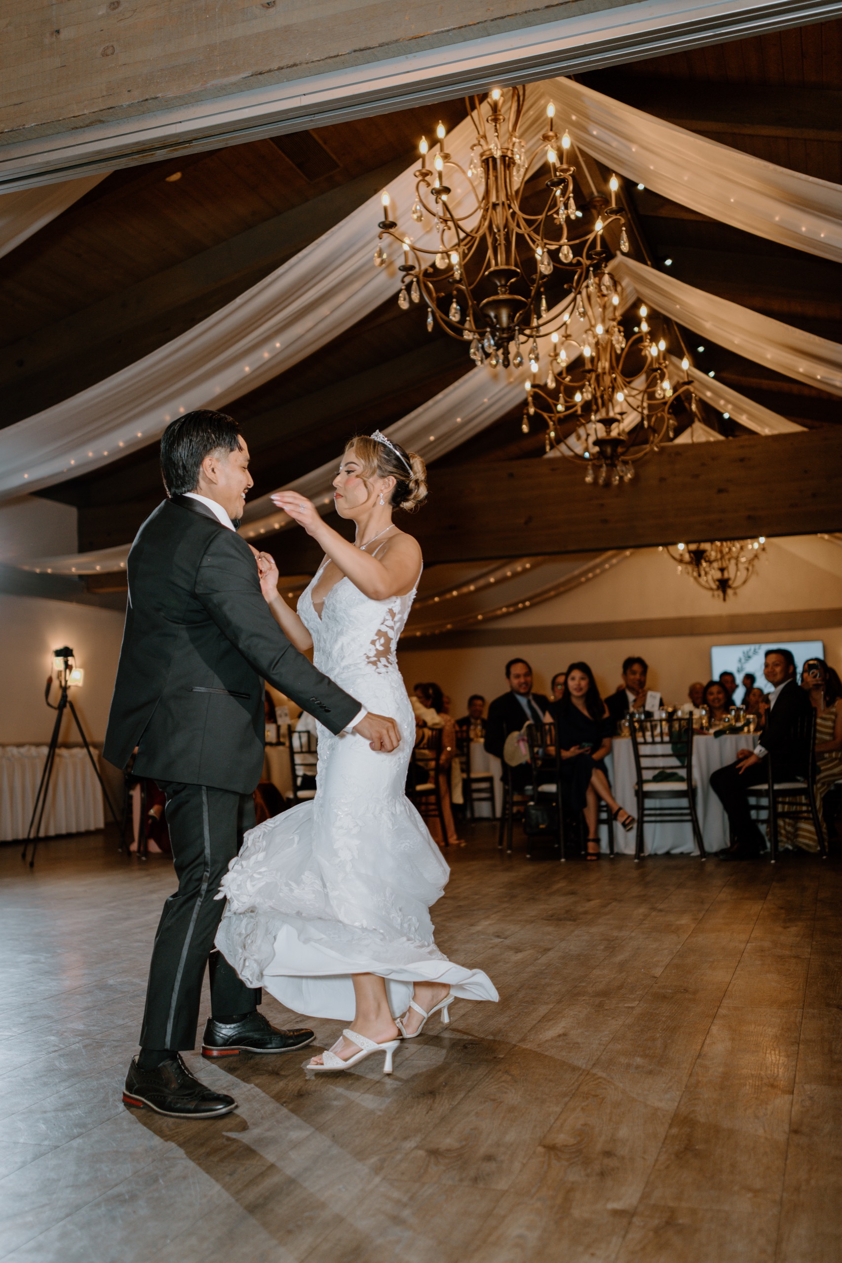 Bride and groom sharing their first dance under chandeliers and draped ceiling lights