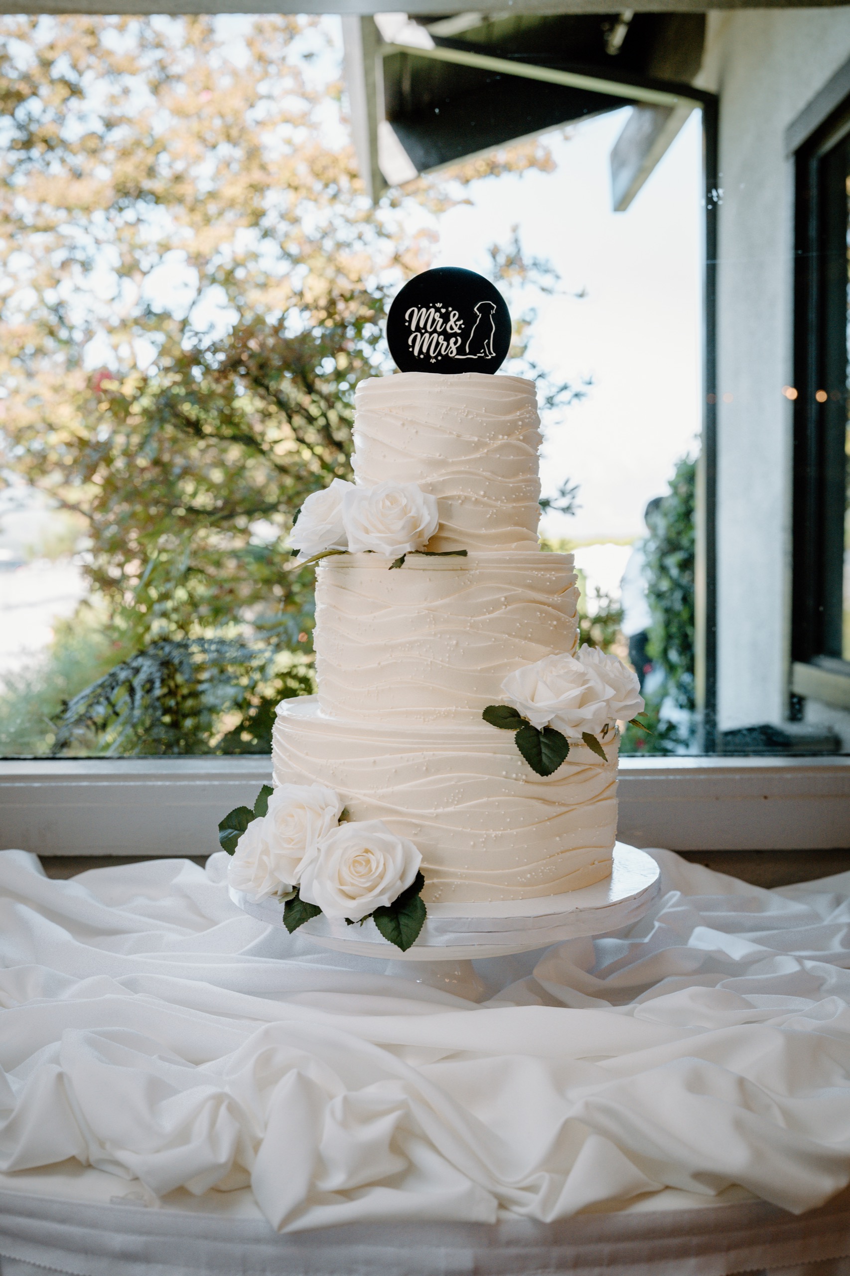 Three-tier white wedding cake with white roses and a Mr & Mrs topper
