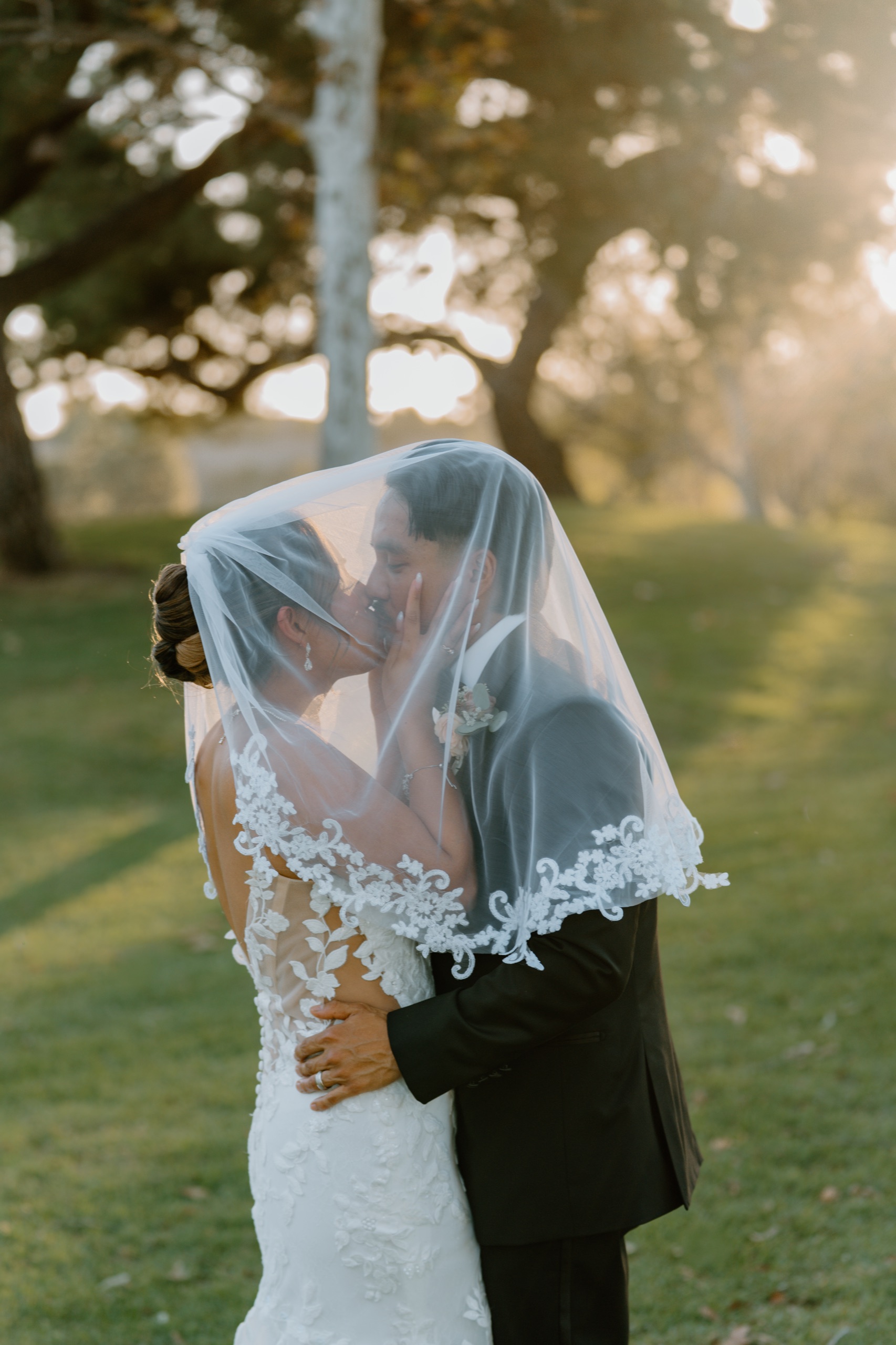 Jane and Jon kissing under her veil in the golden hour light